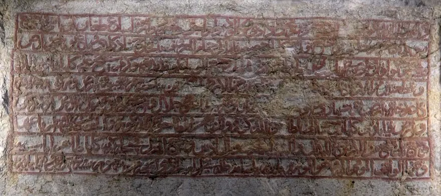 A 600-year-old Ottoman endowment inscription carved directly into natural bedrock has been restored in Amasya, northern Türkiye. Dating to 1418, the Bayezid Pasha foundation text is now readable again after years of damage, and experts say it may represent the only known example of a waqf inscription carved into living rock anywhere in the world.
Located along the banks of the Yeşilırmak River, near the Leğenkaya Waterfall, the inscription had long been obscured by graffiti and surface deterioration. The recent restoration has not only cleaned the stone but also revealed a rare form of Ottoman documentation—one that was literally engraved into the landscape.
A waqf text carved into living rock
Commissioned by Grand Vizier Bayezid Pasha during the reign of Ottoman Sultan Mehmed I, the inscription differs fundamentally from typical waqf documents. Instead of being written on paper or carved onto a separate stone slab, the text was engraved directly into the natural rock surface.
Before carving began, the rock face was carefully leveled to create a smooth plane resembling polished marble. The inscription, executed in relief, spans approximately 3 meters in width and 110 centimeters in height. It consists of eight lines in Arabic script and contains around 125 words, excluding particles.
This deliberate and permanent method of inscription suggests a strong intention to embed the legal and charitable framework of the foundation into the physical environment itself.
From vandalized surface to readable text
Over time, the inscription suffered significant damage. Spray paint, scratches, and informal markings had turned the surface into what locals described as a “writing board,” obscuring much of the original text.
The restoration process involved carefully removing paint residues using a controlled micro-abrasion technique with travertine powder. The weakened stone surface was then stabilized with compatible conservation materials.
To improve legibility, conservators applied subtle shading, allowing the carved letters to stand out more clearly without altering the original structure. As a result, the inscription has regained much of its visual clarity.
Protected for the future
The intervention went beyond cleaning and stabilization. A reinforced protection system was installed around the site, including structural supports and a transparent protective layer over the inscription itself.
Lighting was also added to enhance nighttime visibility, ensuring the inscription can be appreciated while remaining protected from further environmental and human damage.
Why this inscription matters
Waqf (endowment) documents played a central role in the Ottoman world, defining how religious, social, and charitable institutions were funded and maintained. These texts were typically recorded in manuscripts or occasionally inscribed on architectural elements.
The Amasya example stands apart. By carving the endowment directly into bedrock, its creators transformed a legal document into a permanent public statement embedded in the natural landscape.
According to regional heritage officials, this characteristic may make it the only known rock-cut waqf inscription of its kind globally—a claim that, if further supported, would place the monument in a unique position within both Ottoman studies and the broader history of epigraphy.